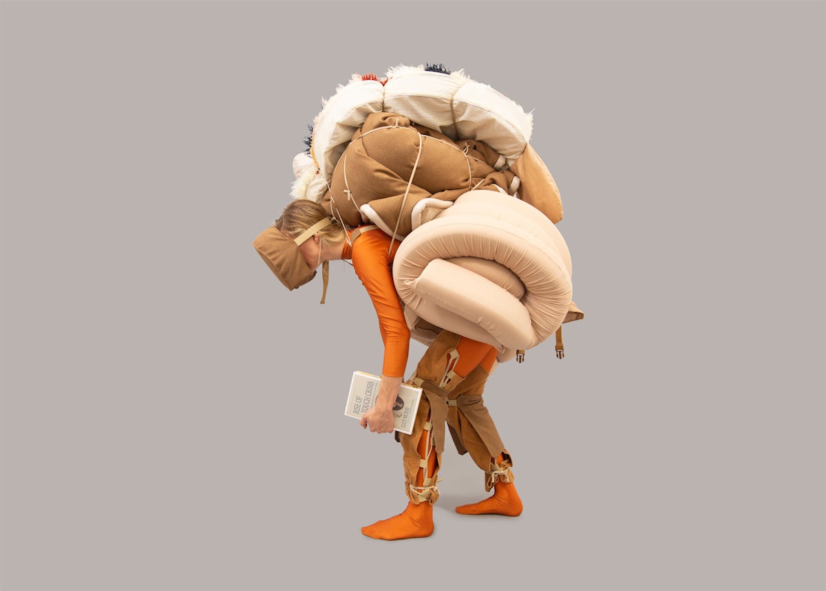 A woman bends under the weight of a large costume
