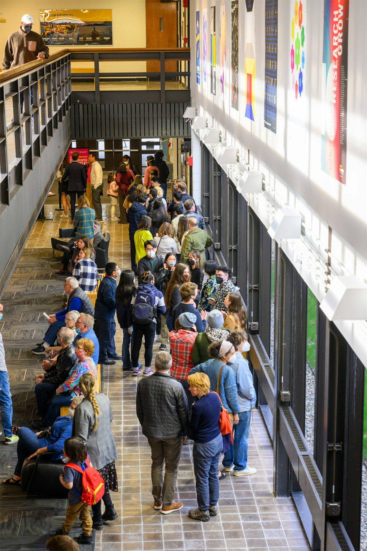 A large number of people, mostly masked, are gathered in the first floor street gallery at the Stamps School.