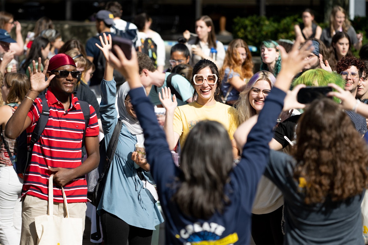 A group of students smile and raise their hands at the 2022 welcome back bash