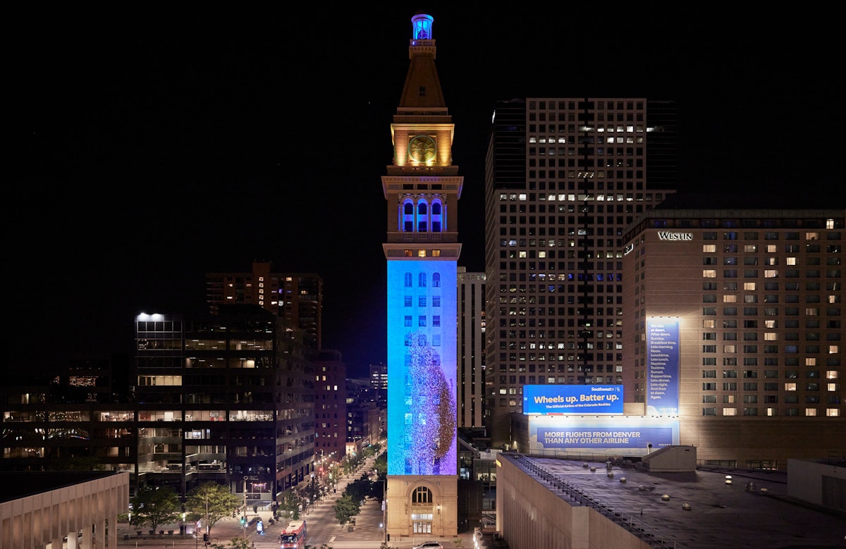 A video of a murmuration of starlings is projected onto a tall clock tower in downtown Denver, CO.