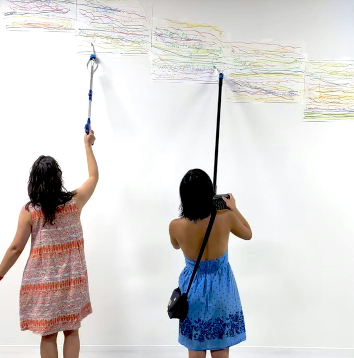 Two figures seen from behind use tools to create marks on paper