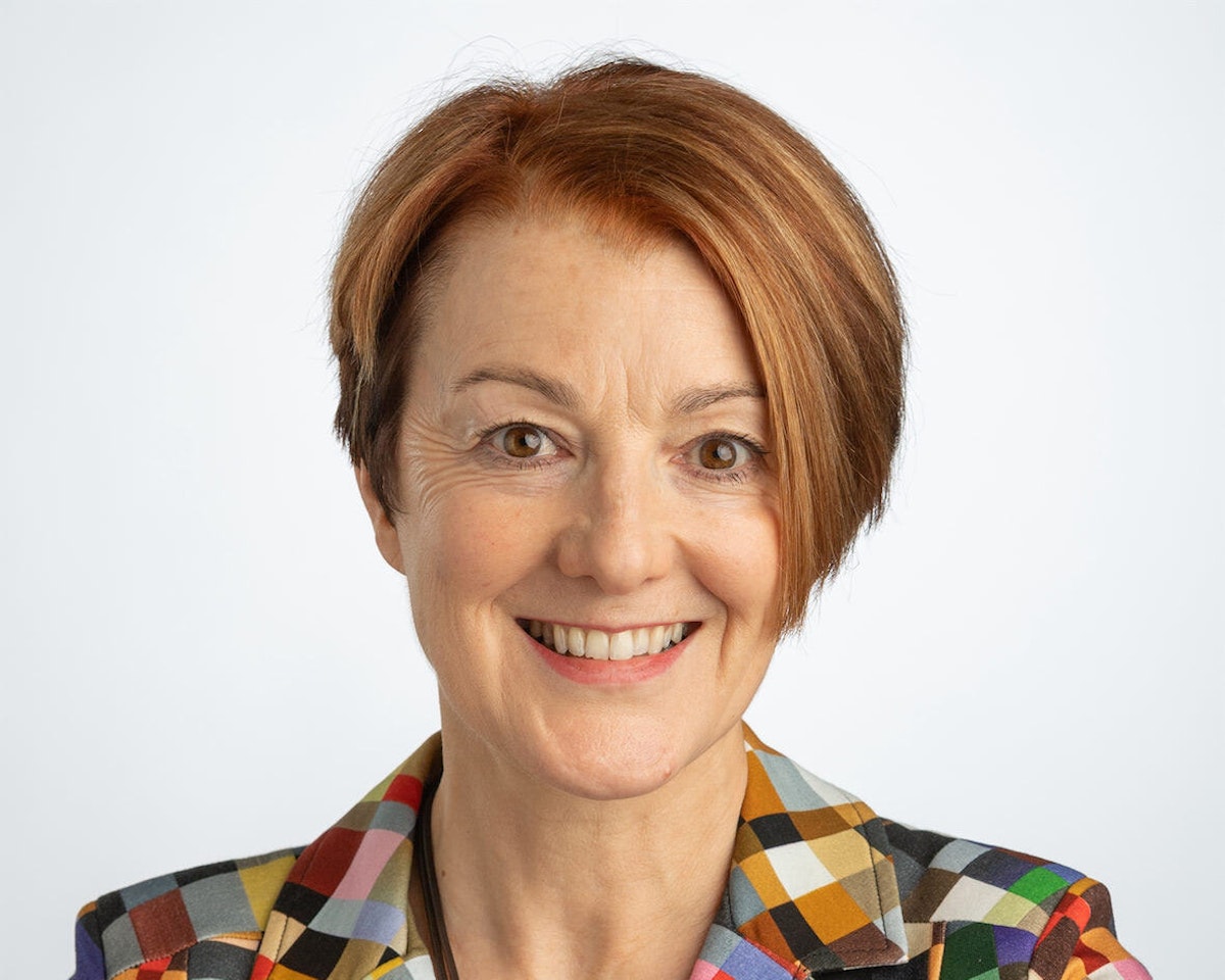 Portrait of Jane Prophet, a woman with red hair wearing a multicolored patterned jacket